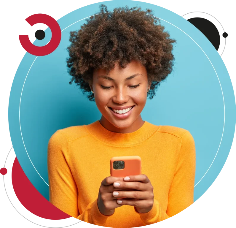 Cheerful good looking woman with Afro hair sends text messages via mobile phone dressed casually in orange sweater.